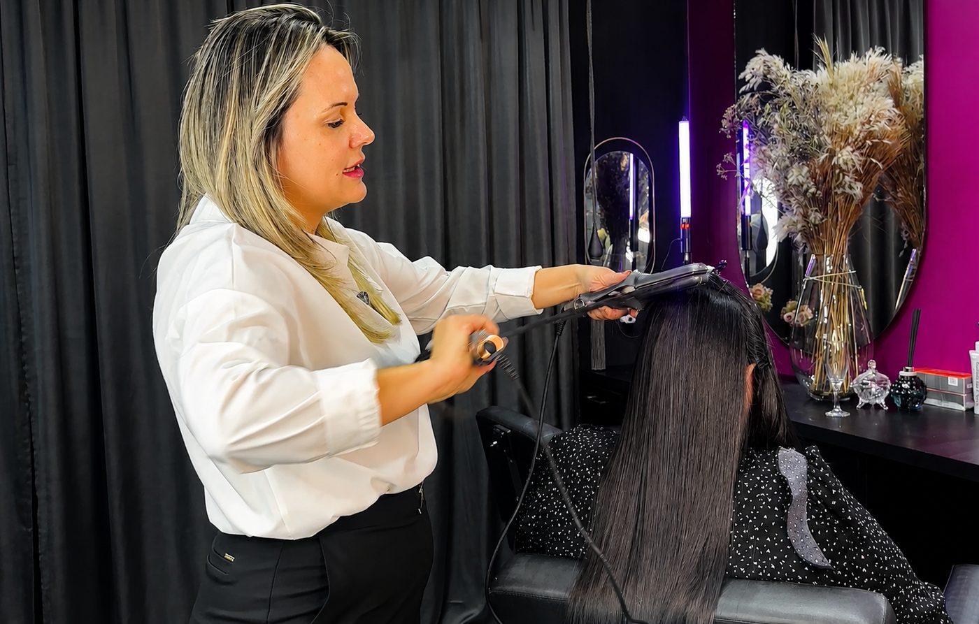 Cabeleireira sorrindo ao lado de cliente com cabelo liso